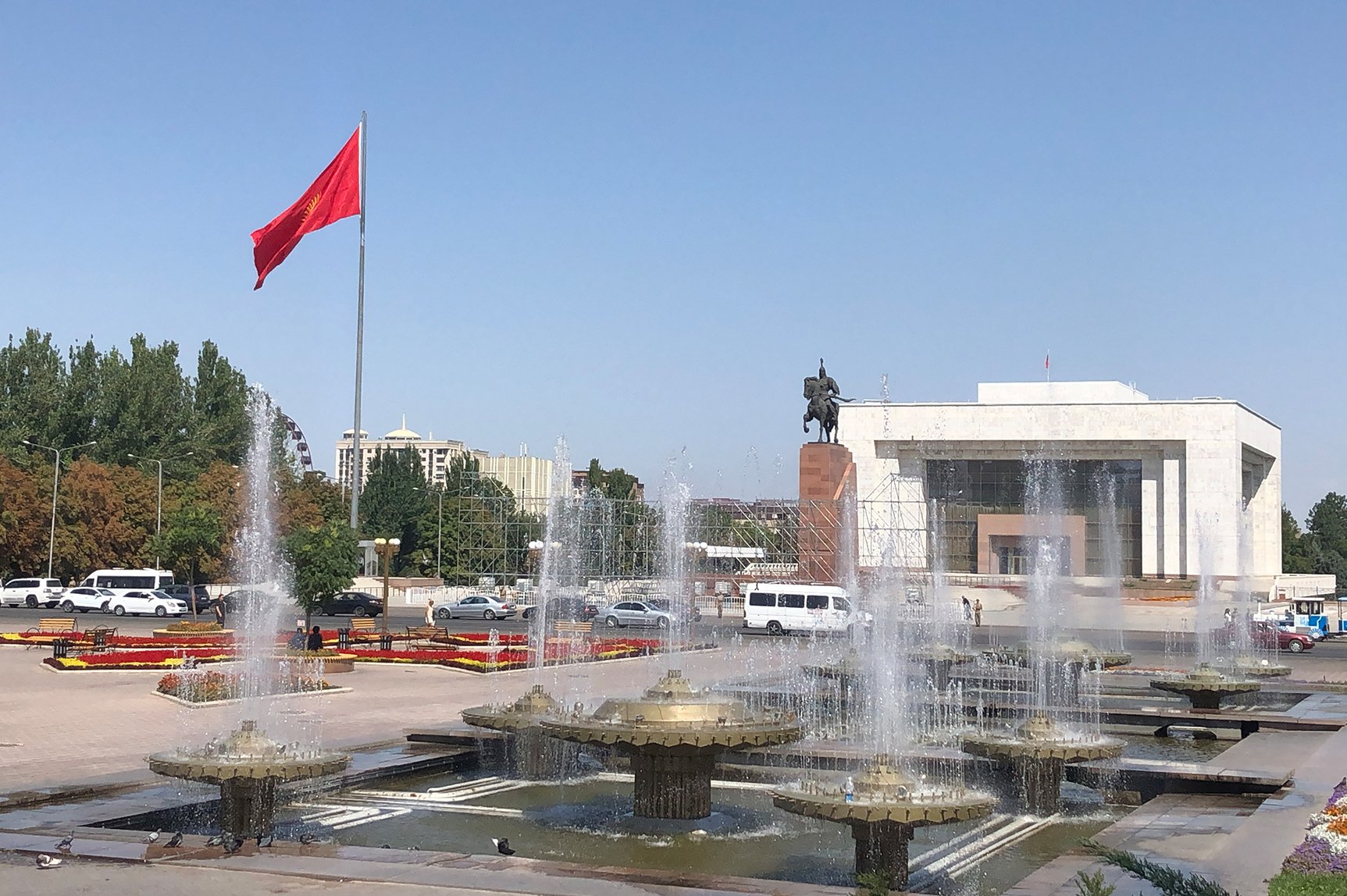 Ala Too Square Bishkek, the capital of the Kyrgyz Republic, on a very sunny, cloudless day. There are fountains and a large Kyrgyz flag on a tall flagpole billowing. (Photo: Emil Akhmatbekov)