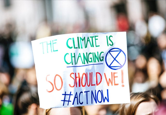 Person holding climate change sign with Extinction Rebellion symbol. (Photo: Markus Spiske/Unsplash)