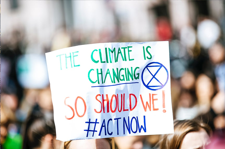 Person holding climate change sign with Extinction Rebellion symbol. (Photo: Markus Spiske/Unsplash)