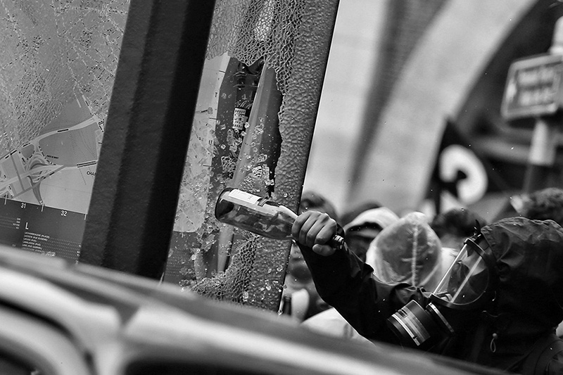 Protester smashing a window with a bottle (Photo credit: Randy Colas/Unsplash)