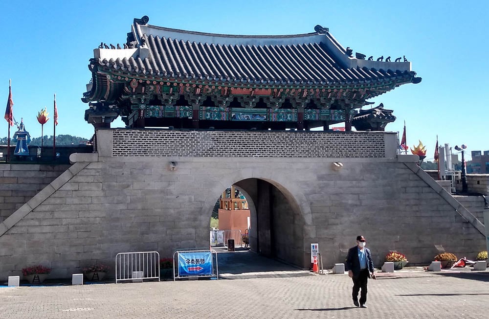 A man with a mask walks in front of a traditional gate in South Korea