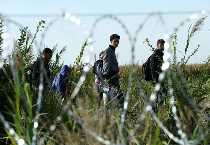 Migrants in hungary with barb wire fence (photo credit: Gémes Sándor/SzomSzed/Wikimedia)