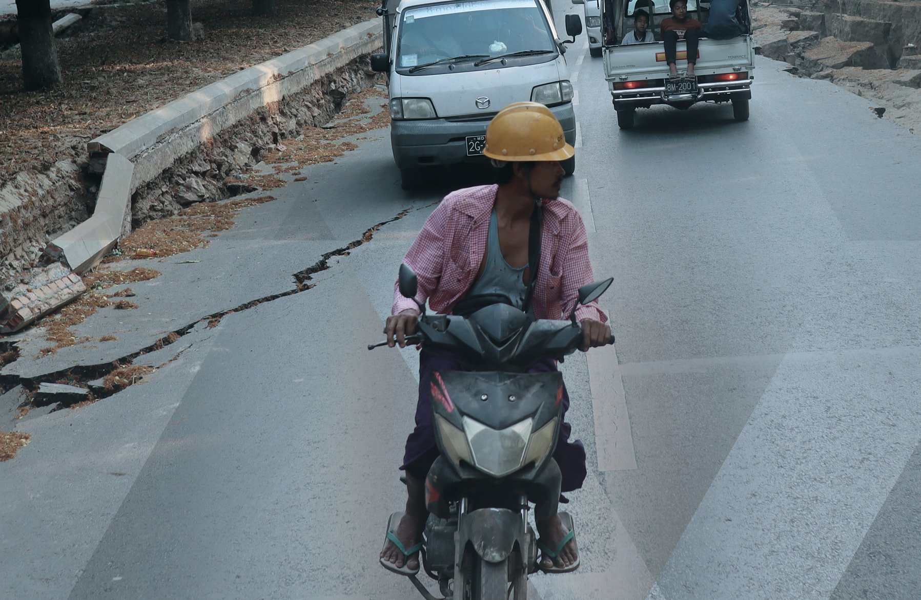Photo of cars and a man riding a motorbike in the aftermath of the 2025 Myanmar earthquake, with damage visible on the road