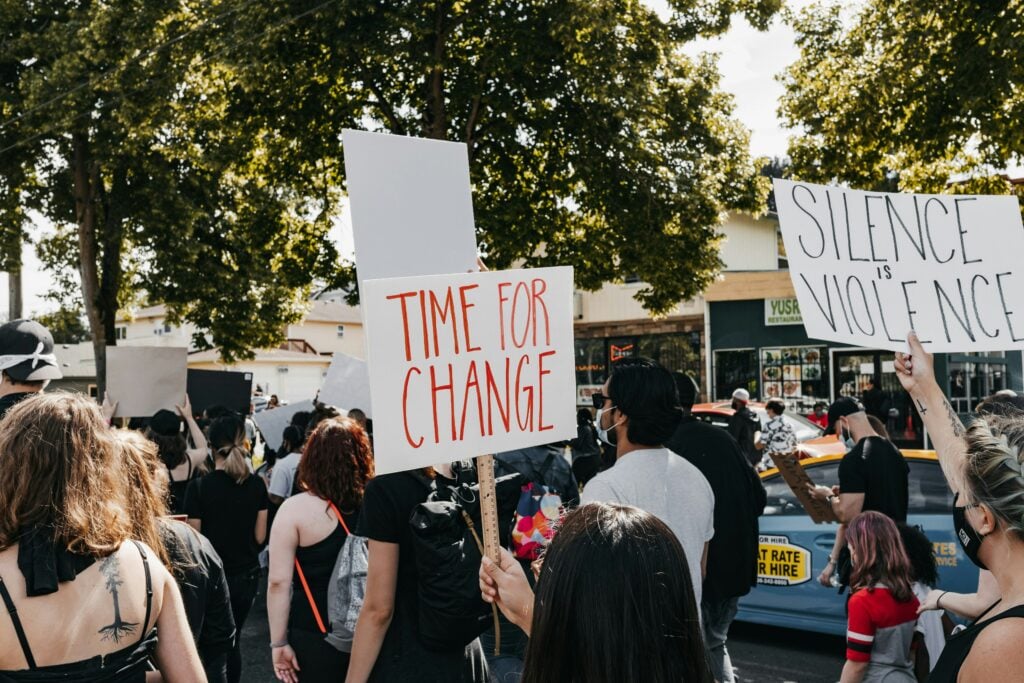 Crowd marching with signs that read "TIME FOR CHANGE" and "SILENCE IS VIOLENCE"