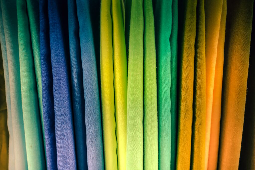 Photo of multi-color fabrics taken in Saida, Lebanon. The fabrics are draped vertically, and are teal, blue, yellow, green, orange, and yellow. Women in civil society. (Photo: Jametlene Reskp/Flora Saltzmann/Unsplash)