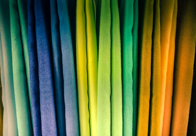 Photo of multi-color fabrics taken in Saida, Lebanon. The fabrics are draped vertically, and are teal, blue, yellow, green, orange, and yellow. (Photo: Jametlene Reskp/Flora Saltzmann/Unsplash)