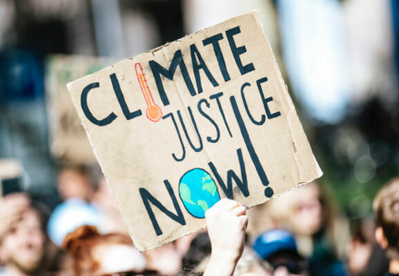 Cardboard sign at protest that says Climate Justice Now (photo credit: unsplash.com)