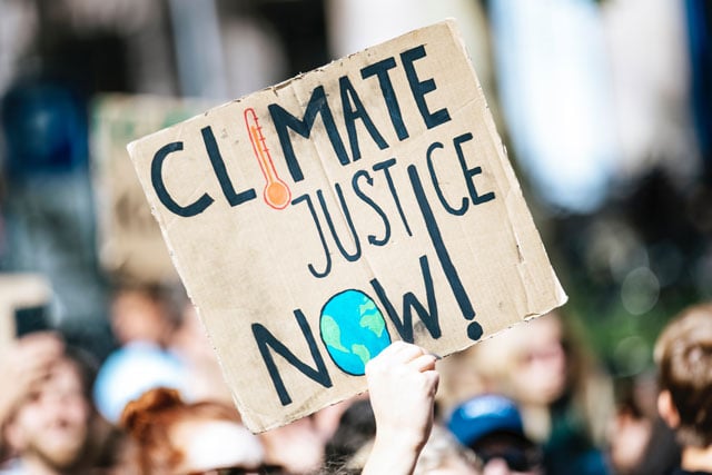 environmental defenders; Cardboard sign at protest that says Climate Justice Now (photo credit: unsplash.com)