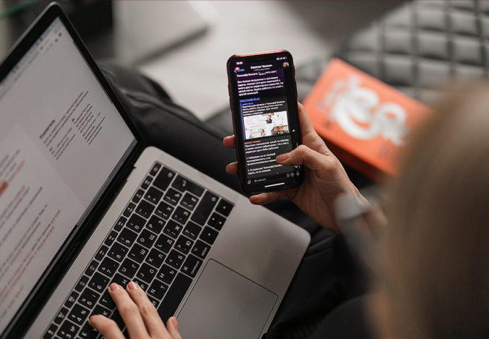 Young woman on leather couch working at a laptop while browsing her phone (Photo: Maxim Ilyahov on Unsplash)