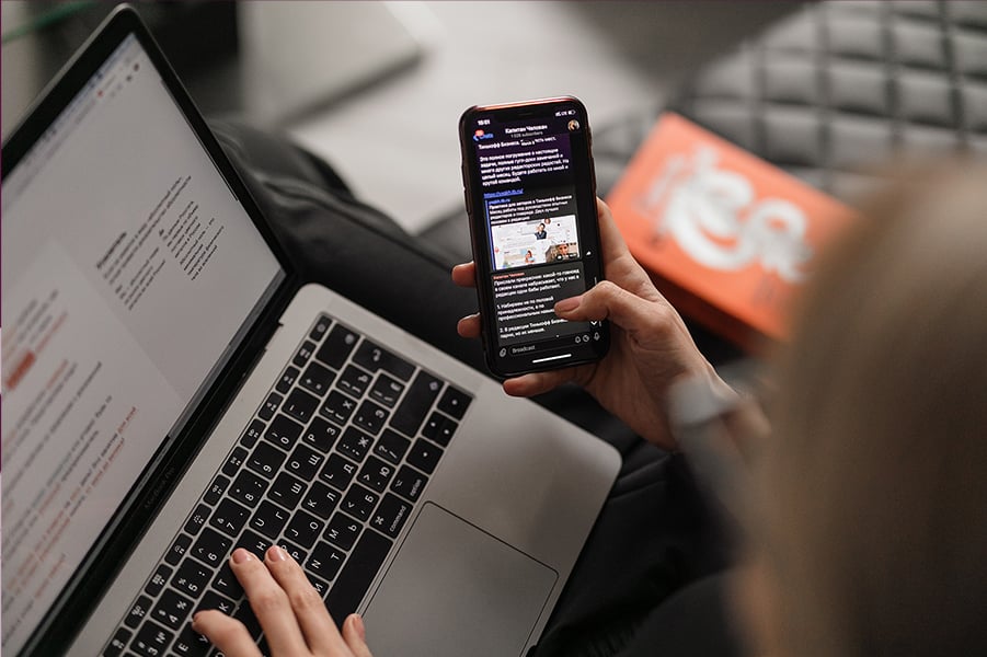 Bread&Net; Young woman on leather couch working at a laptop while browsing her phone (Photo: Maxim Ilyahov on Unsplash)